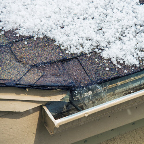 damaged shingle roof covered in hailstones